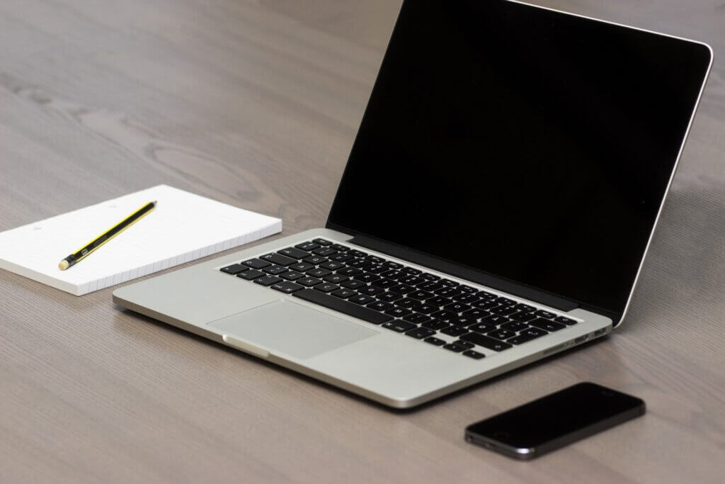 Auf dem Bild befindet sich ein Block mit einem Stift, ein Laptop und ein Smartphone.